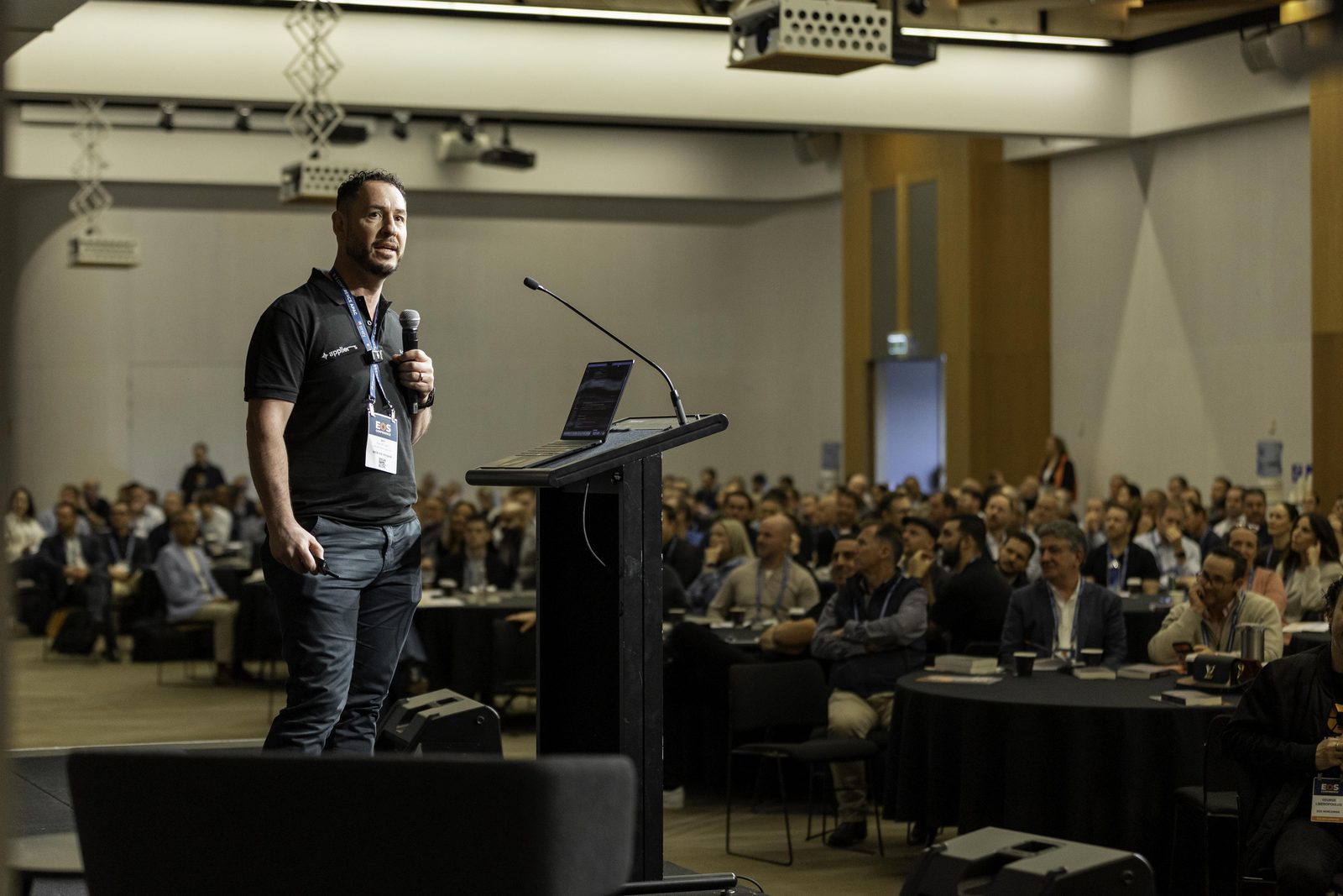 Pete Gatt speaking on the main stage with the full room seated in front of him.