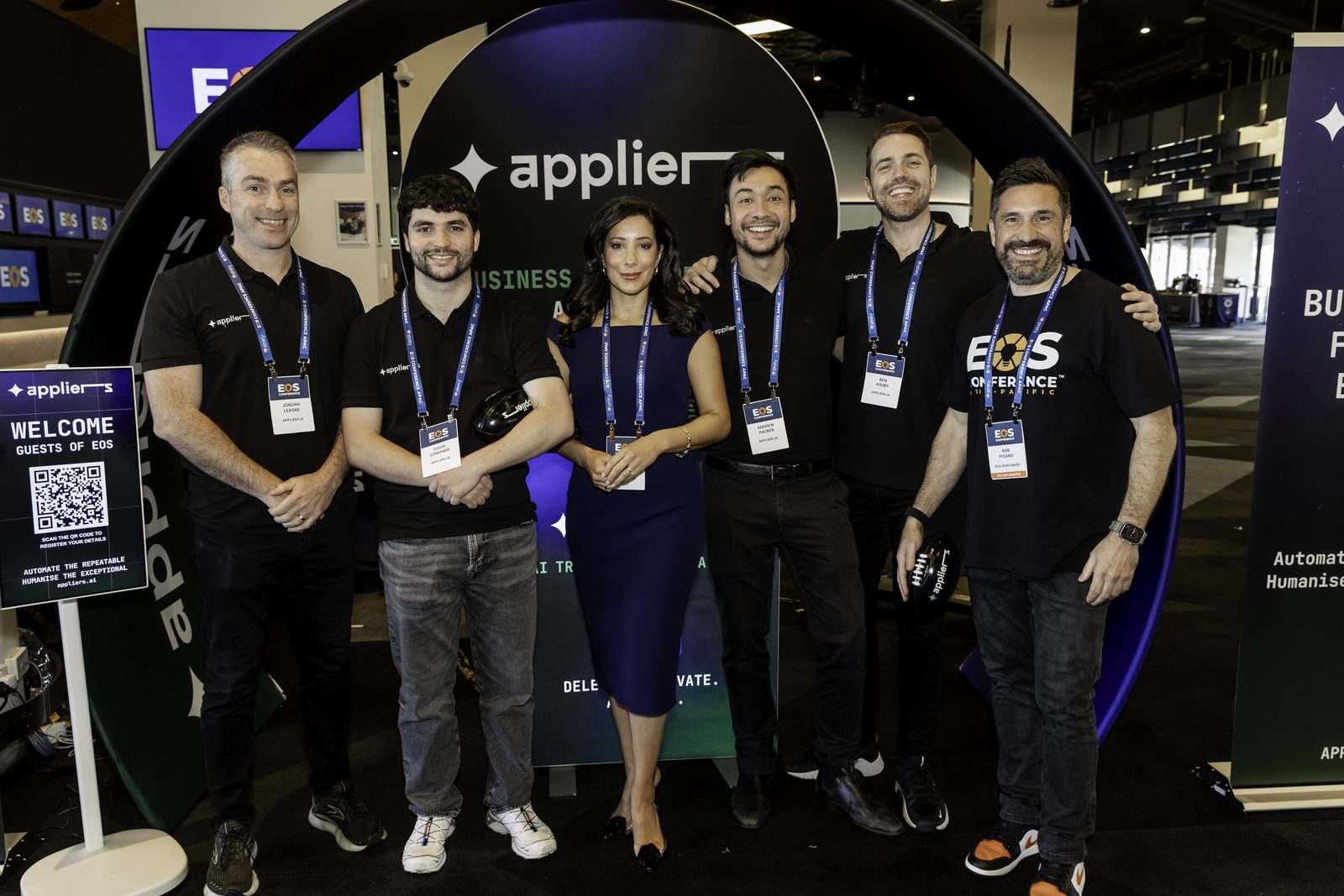 Six members of the Appliers team standing together in branded black polos in front of the Appliers arch on the expo floor.